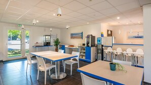 Un espace repas moderne, équipé de tables et de chaises, d’un distributeur d’eau et d’une machine à café.