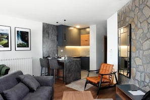 A modern living room with a grey sofa, a brown leather chair, and a kitchen area with a bar counter. - Zlatibor Residence & Suite (Zlatibor)
