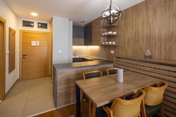 A modern kitchen with wooden cabinetry, a dining area with a wooden table and chairs, and a pendant light above the island. - Zlatibor Residence & Suite (Zlatibor)