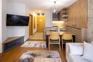 A modern living room with a flat-screen TV, a dining area with a table and chairs, and a kitchen with wooden cabinets. - Zlatibor Residence & Suite (Zlatibor)