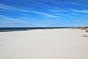Una playa extensa de arena clara, con cielo azul y mar tranquilo.