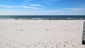 A beach with footprints leading to the water, a red lifeguard chair, and a clear sky. - Coastal Gulf Front Studio in Fort Morgan | Sleeps 4 (Gulf Shores)