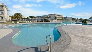 En swimmingpool med gelænder, omgivet af en betonflisebelægning og en bygning med balkoner i baggrunden.