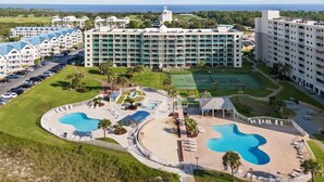 Et hotel med flere bygninger, et stort poolområde og en tennisbane.