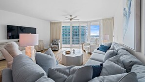 Ein modernes Wohnzimmer mit einer Couch, einem Couchtisch, einem Fernseher und Blick auf ein Gebäude durch große Fenster.