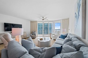 Ein modernes Wohnzimmer mit einer Couch, einem Couchtisch, einem Fernseher und Blick auf ein Gebäude durch große Fenster.