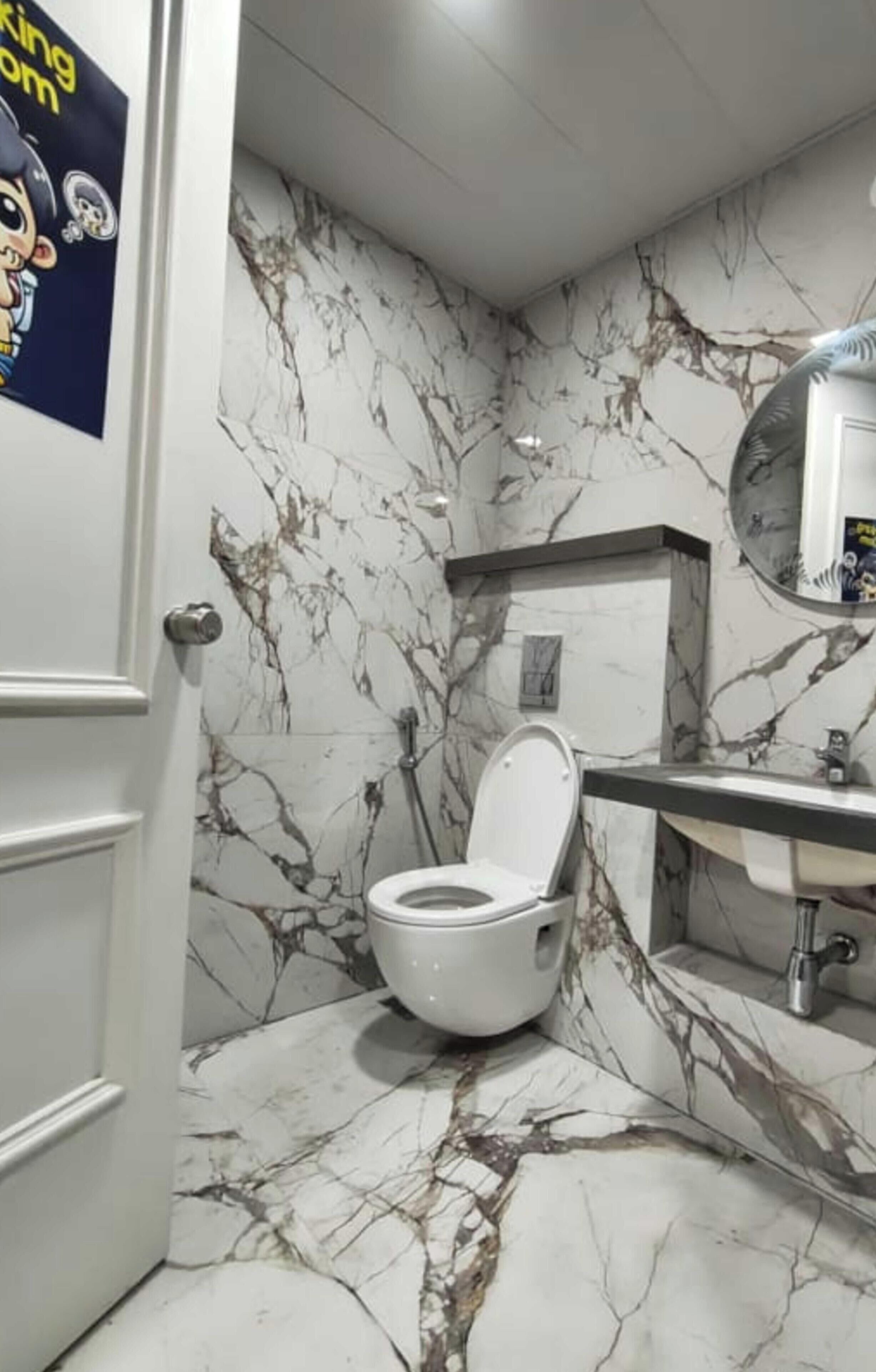 A bathroom with a toilet, a sink, a mirror, and a marble-patterned wall.