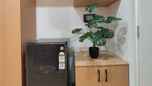 Una cocina compacta con refrigerador, una planta en maceta y armarios de madera.