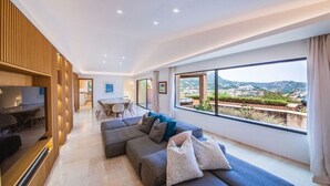 A modern living room with a large sofa, a TV, and a dining area with a table and chairs. - Villa Hermes - Porto Cervo Center (Porto Cervo)