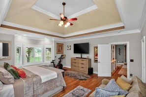 A bedroom with a bed, a TV, a ceiling fan, and a view of the outside.