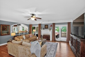 A living room with a sofa, coffee table, fireplace, television, and a ceiling fan.