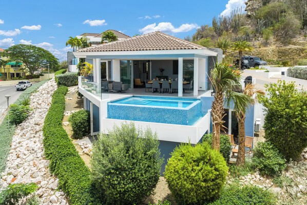 Ein modernes Haus mit Schwimmbad, überdachter Terrasse und Blick auf die umliegende Landschaft.