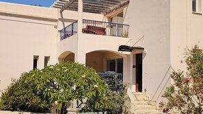 Un edificio a due piani con un balcone, una zona esterna coperta e una scala che conduce all'ingresso.