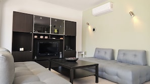 A modern living room with a dark wood cabinet, a flat-screen TV, a grey sofa, and a coffee table. - Casa Elysia 3BR with beach and pool (Platanias)