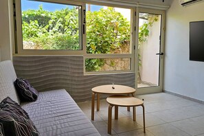 A room with a sofa, two small round tables, and a large window with a view of greenery.