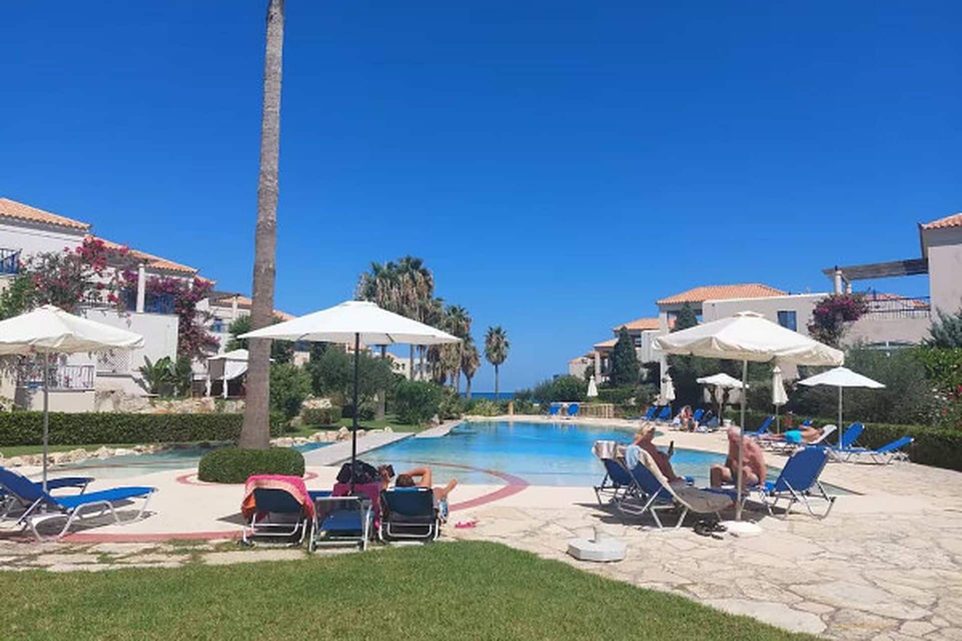 Zona de piscina amb gandules i ombrelles, envoltada d'edificis amb teules vermelles.