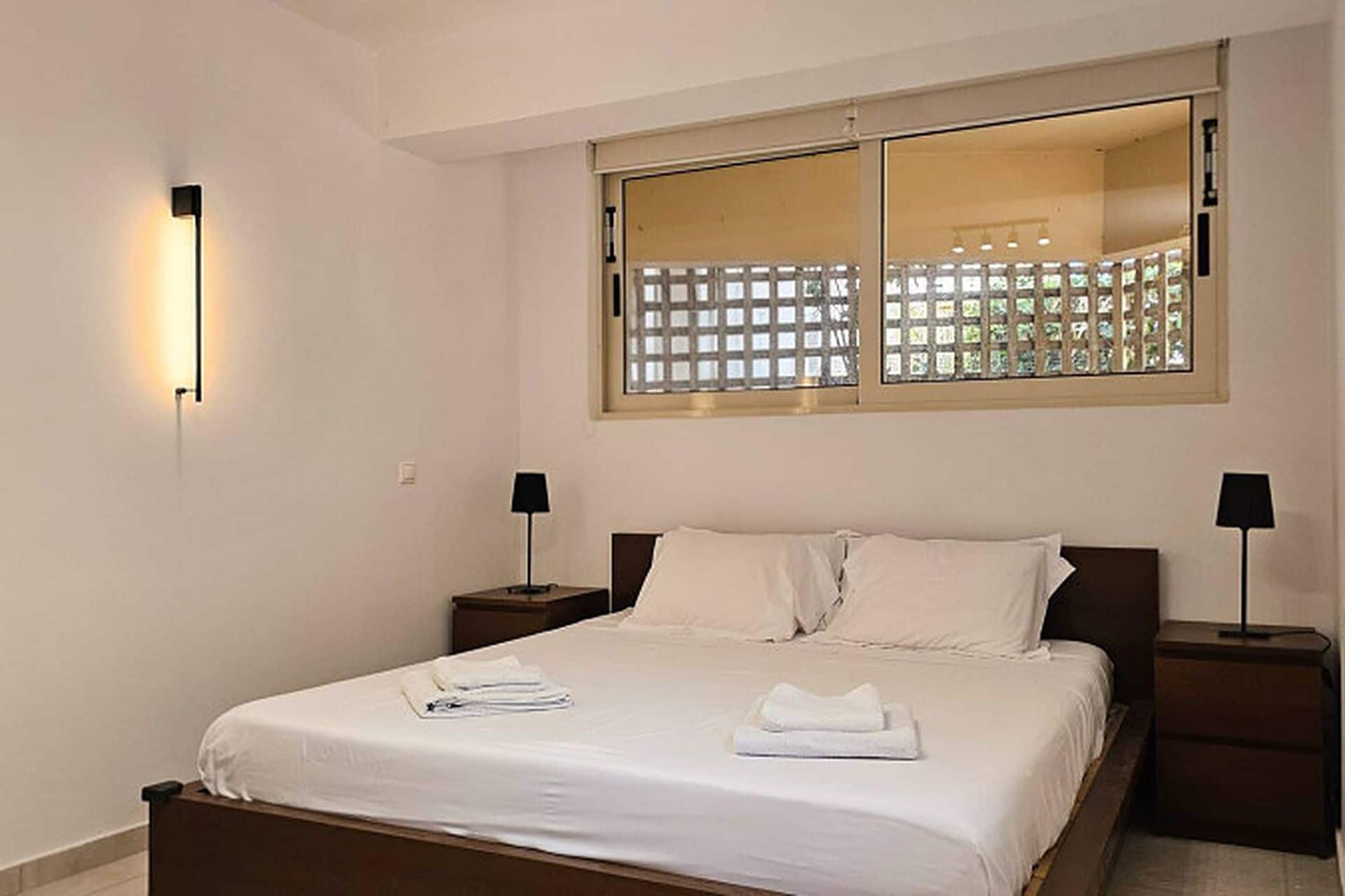 A hotel room with a large bed, two bedside tables, a window with a view, and a wall-mounted light fixture.