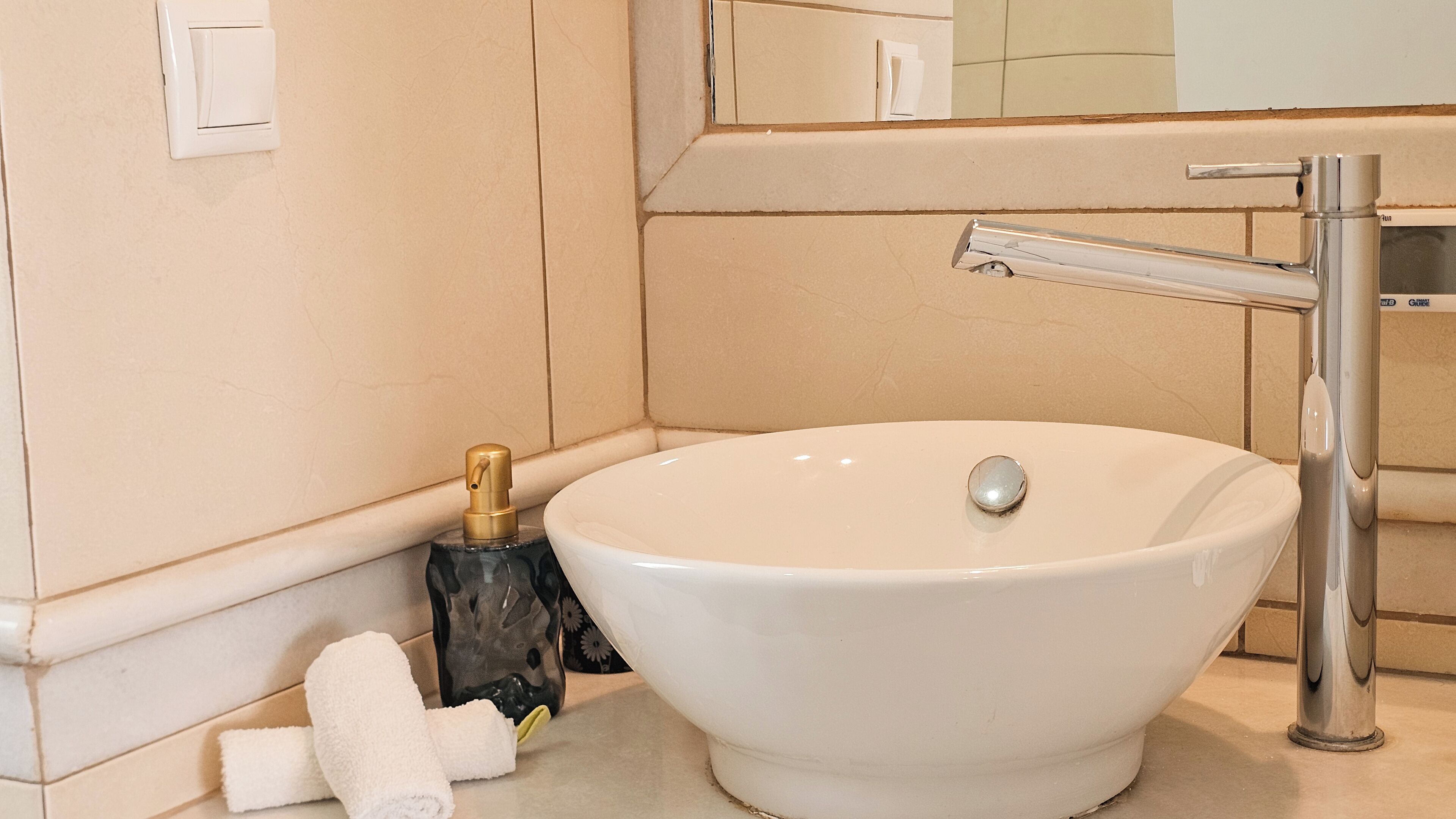 Un baño con un lavabo blanco, un espejo, una toalla y una botella.