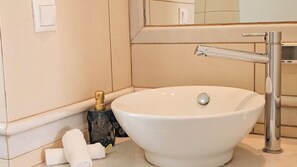 Une salle de bain avec un lavabo blanc, un miroir, une serviette et une bouteille.