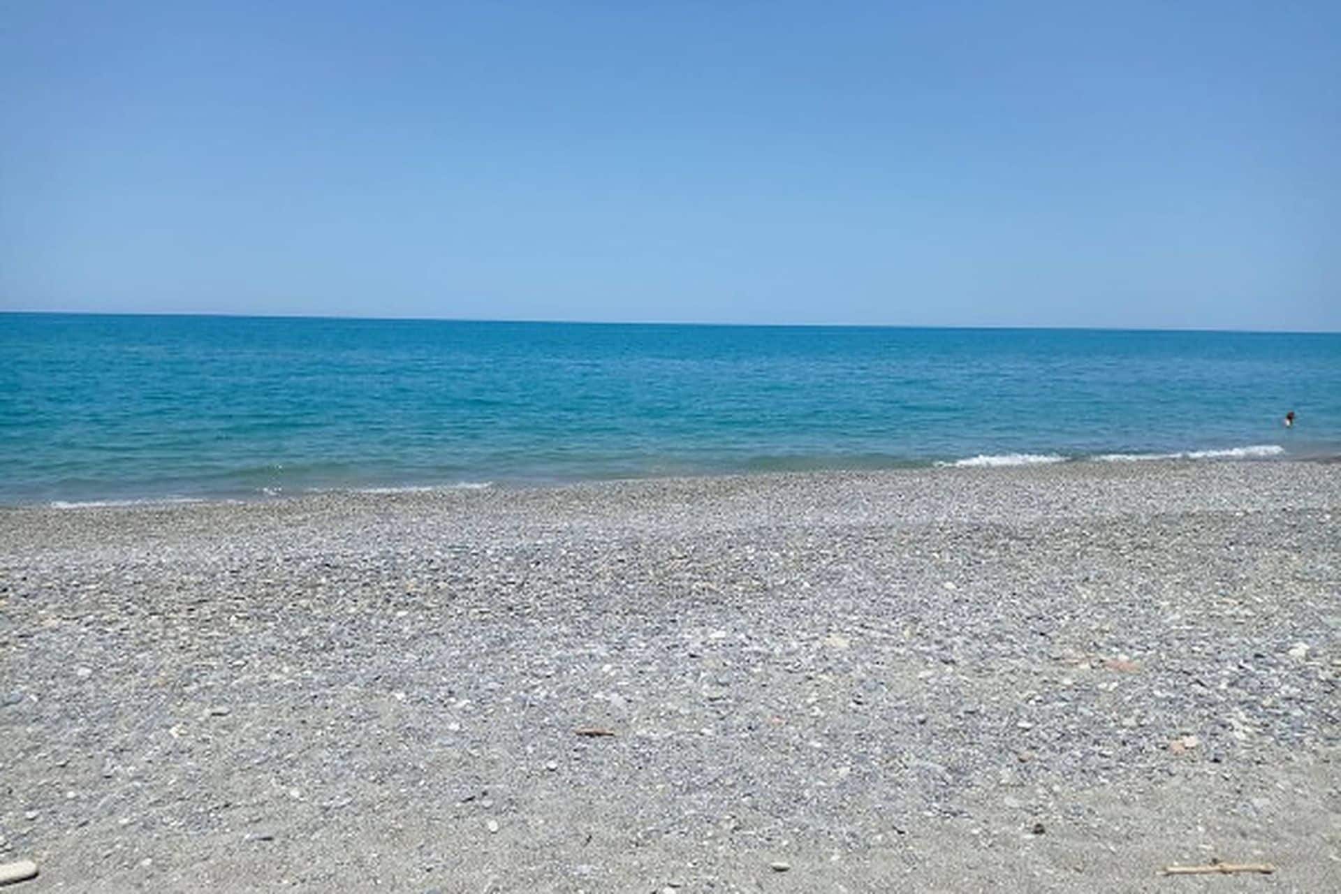 Ein Kiesstrand mit blauem Himmel und ruhiger See.