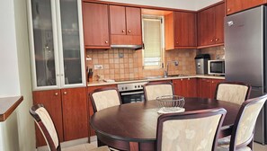 Une cuisine avec des meubles en bois, un réfrigérateur en acier inoxydable, un four encastré et une table à manger avec des chaises.