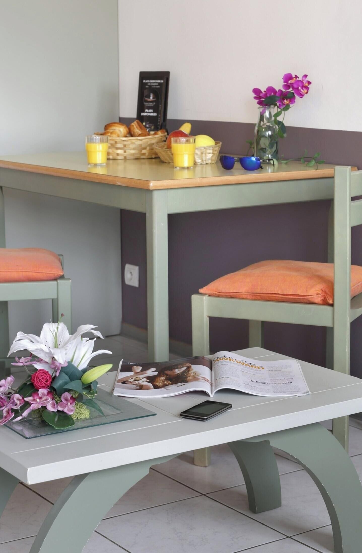 A dining table with a book, a smartphone, and a vase of flowers.