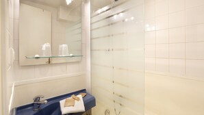 Ein Badezimmer mit Duschkabine aus Glas, einem blauen Waschbecken und einem Spiegel mit Glasablage.