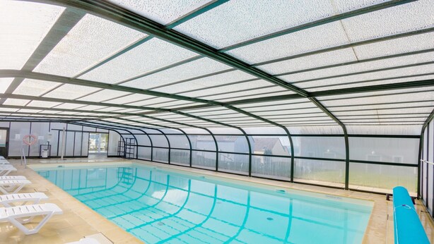 An indoor swimming pool with clear water, surrounded by white lounge chairs and a glass ceiling. - Saint-nic Retreat Near Beach (Saint-Nic)