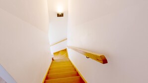 A staircase with wooden steps and a wooden handrail, leading to a landing with a light fixture. - Saint-nic Retreat Near Beach (Saint-Nic)
