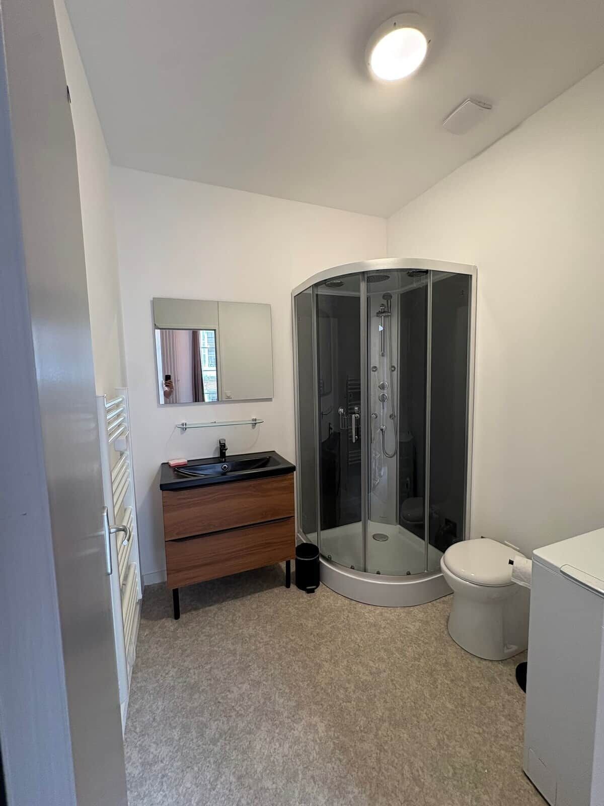 Un baño moderno con ducha de vidrio, lavamanos con espejo e inodoro.