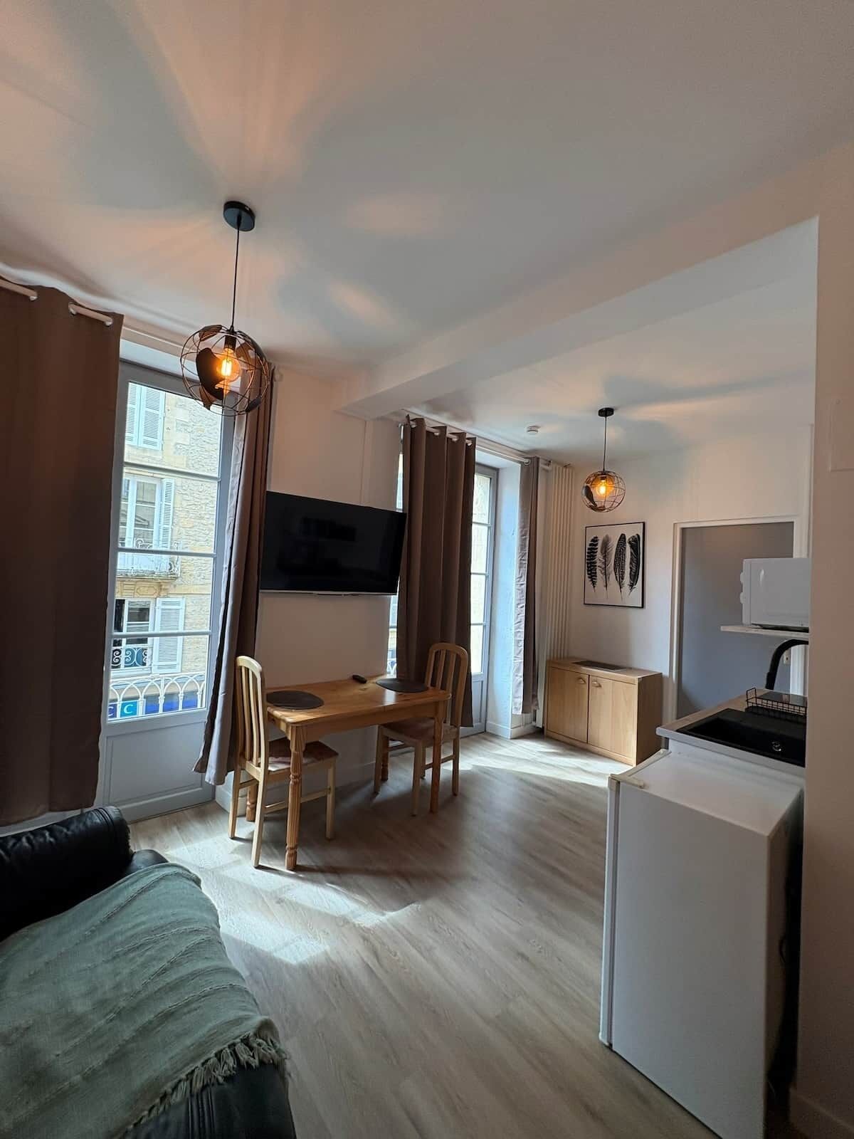 Un espacio habitable compacto con comedor, kitchenette y televisor montado en la pared.