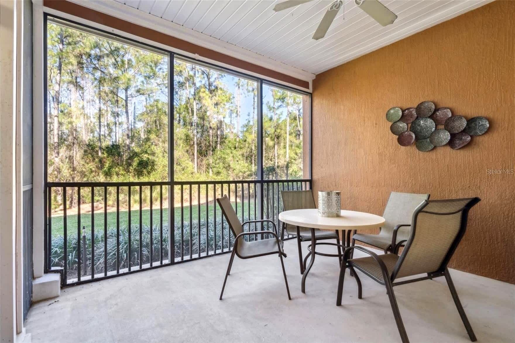 A balcony with a table and chairs, a view of a golf course, and a decorative wall piece.