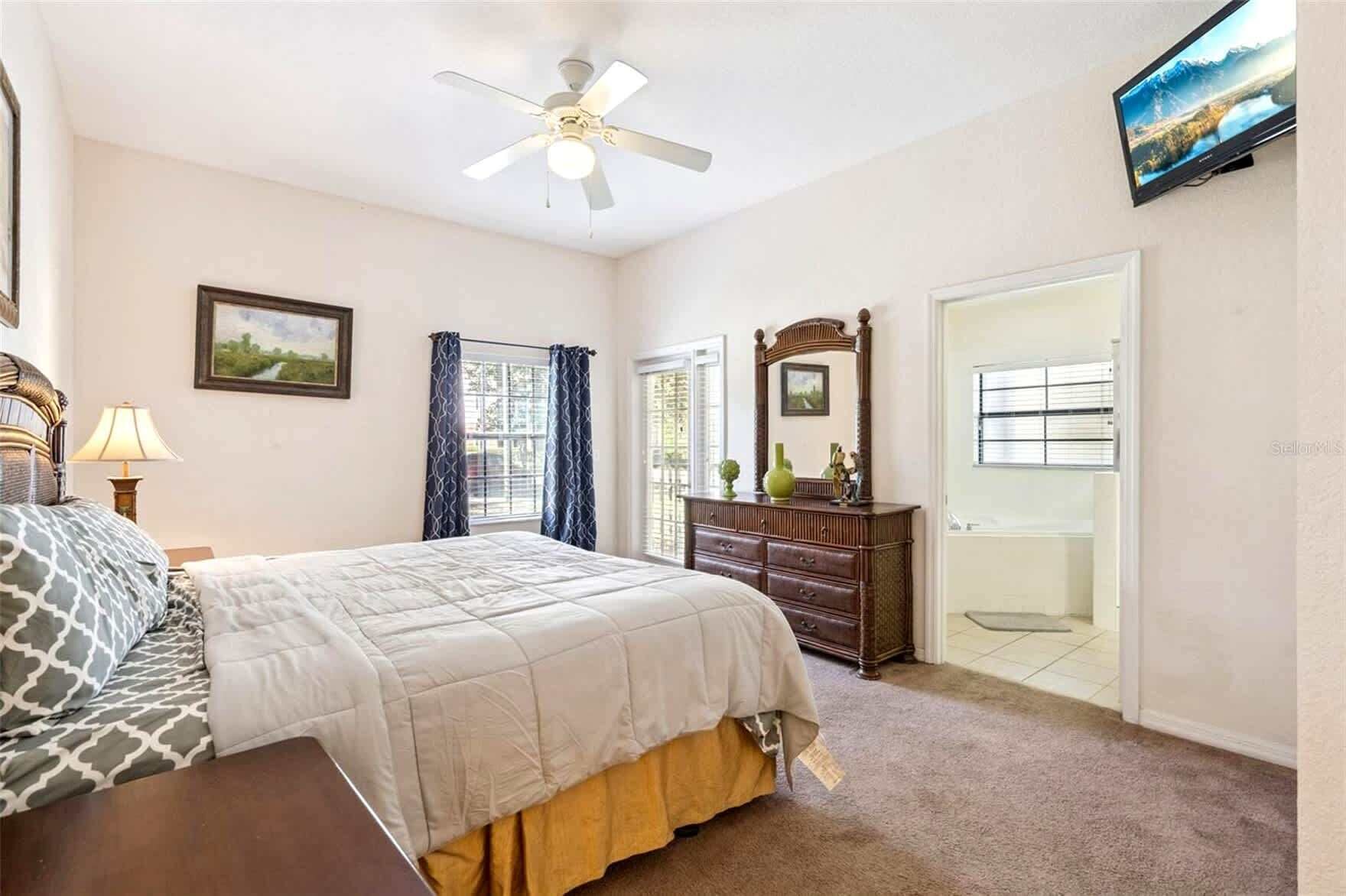 Une chambre à coucher avec un lit, une commode, un miroir et un téléviseur fixé au mur.