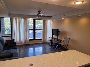 Ein Wohnzimmer mit einer Couch, einem Flachbildfernseher, einem Deckenventilator und einem Fenster mit Vorhängen.