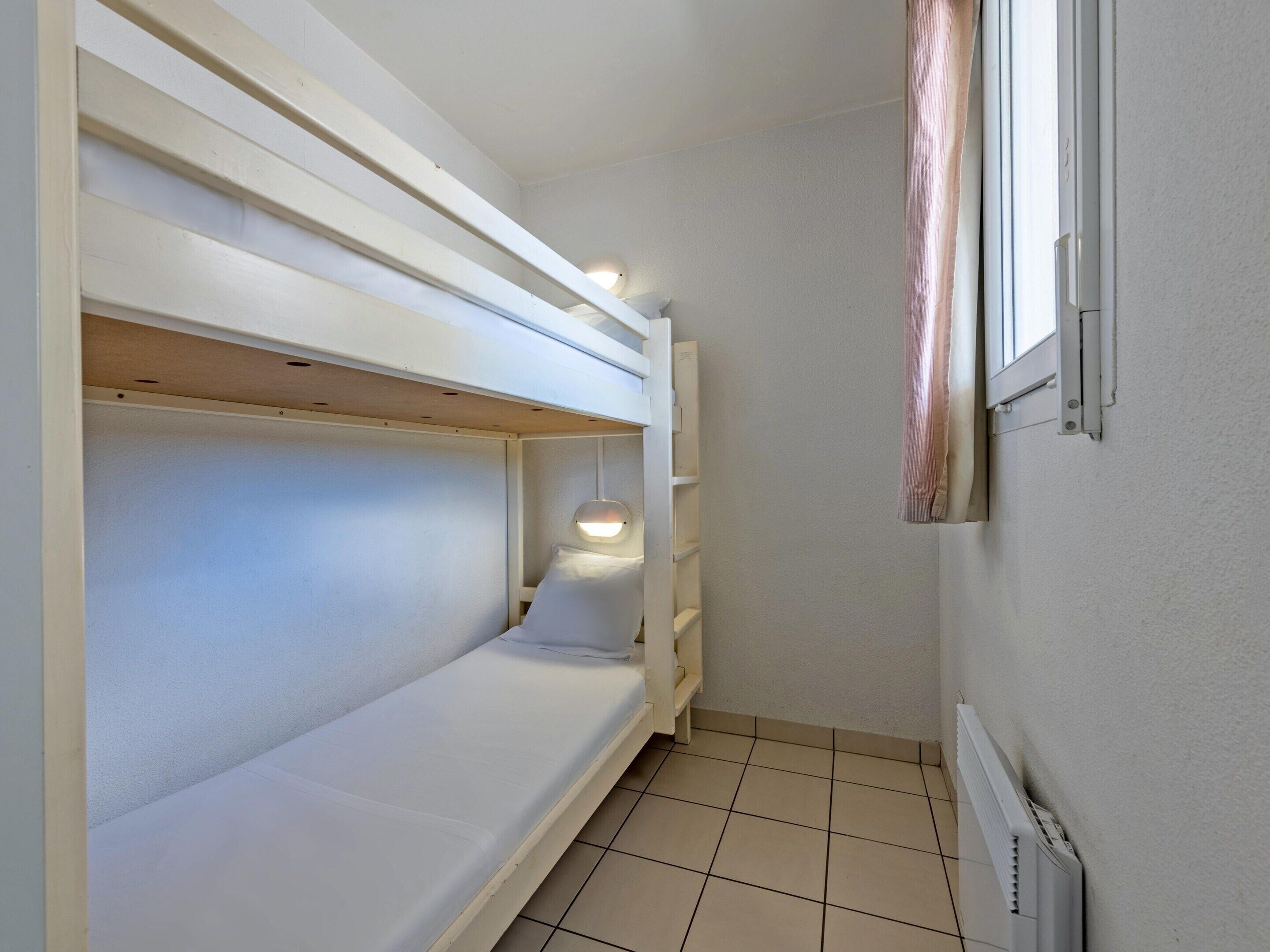 Een kleine kamer met stapelbedden, een raam met gordijnen en een radiator.