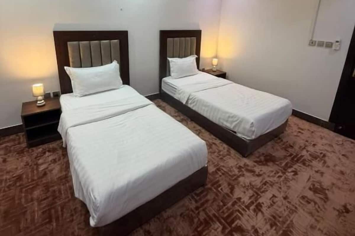 A hotel room with two beds, a carpeted floor, and a wall-mounted light fixture.