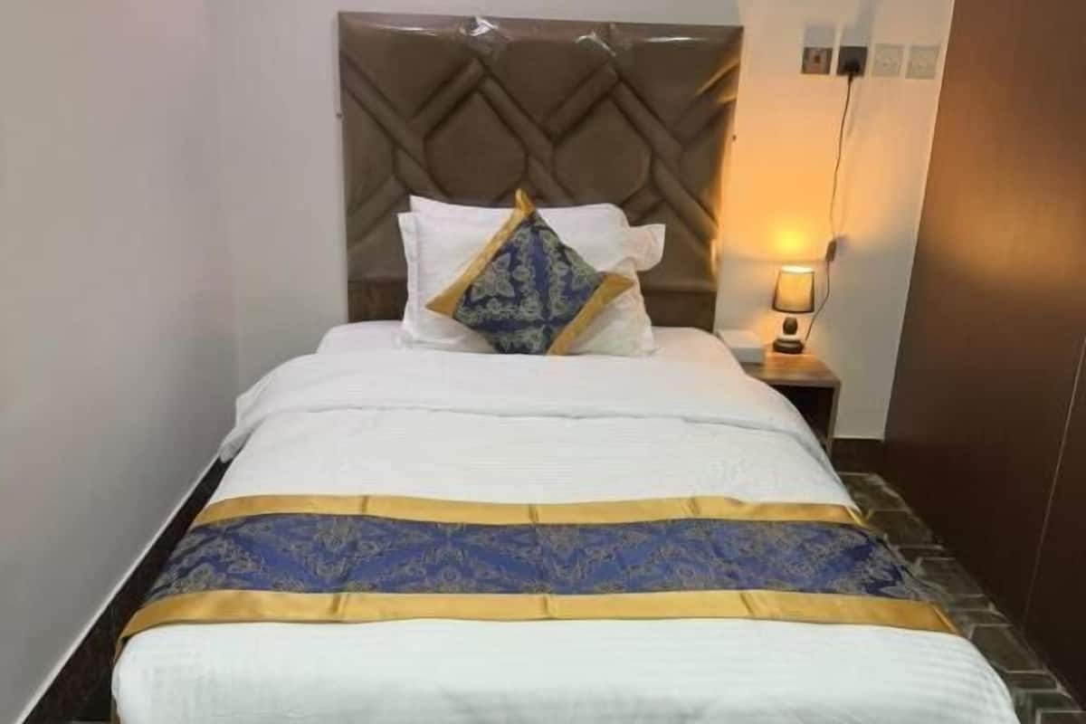 A hotel room with a bed, a headboard, a bedside table with a lamp, and a patterned floor.