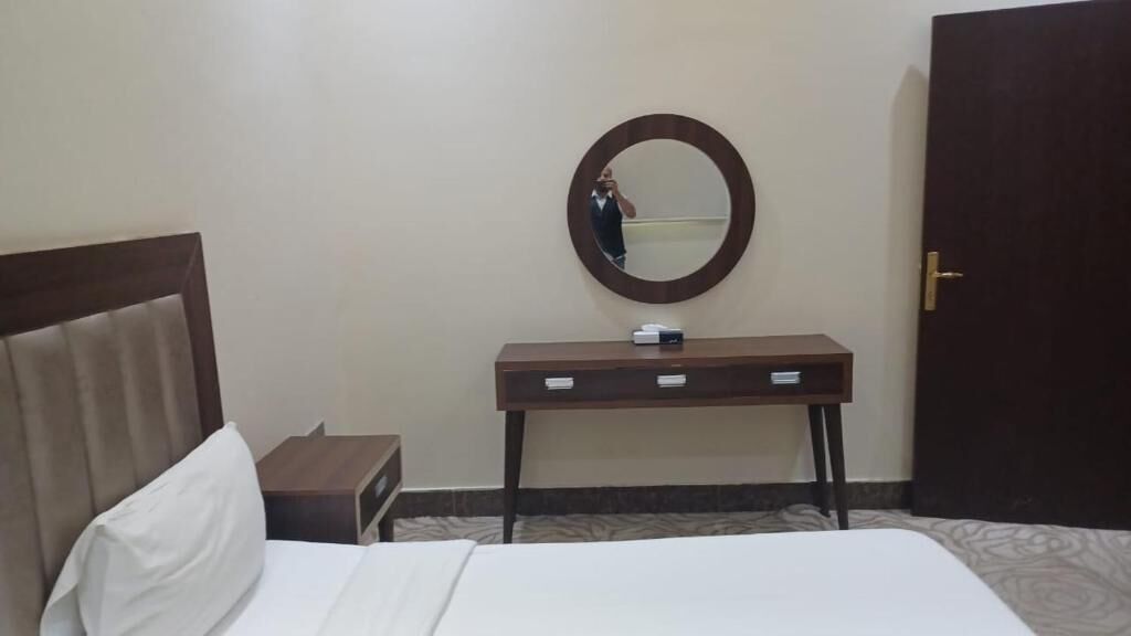 Ein Hotelzimmer mit einem Bett, einem Nachttisch, einem Spiegel, einer Kommode und einer Tür.