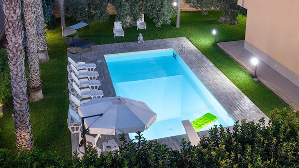 A rectangular swimming pool with lounge chairs and umbrellas, surrounded by well-maintained grass and palm trees. - Spacious Coastal Villa With Pool in Scicli (Scicli)