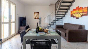 A dining area with a table set for two, a sofa, a TV, and a staircase. - Spacious Coastal Villa With Pool in Scicli (Scicli)