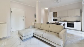 A modern living room with a beige sectional sofa, a white door, and a kitchen area in the background. - Bright and spacious apartment of approximately 80 square meters, perfect for four people, located on the first floor of a building with an elevator (NOT accessible to disabled guests).The property is located in the Sampierdarena neighborhood, one of the  (Genova)