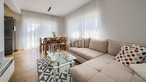 Una sala moderna con un sofá, una mesita de vidrio, una mesa de comedor con sillas y un refrigerador.