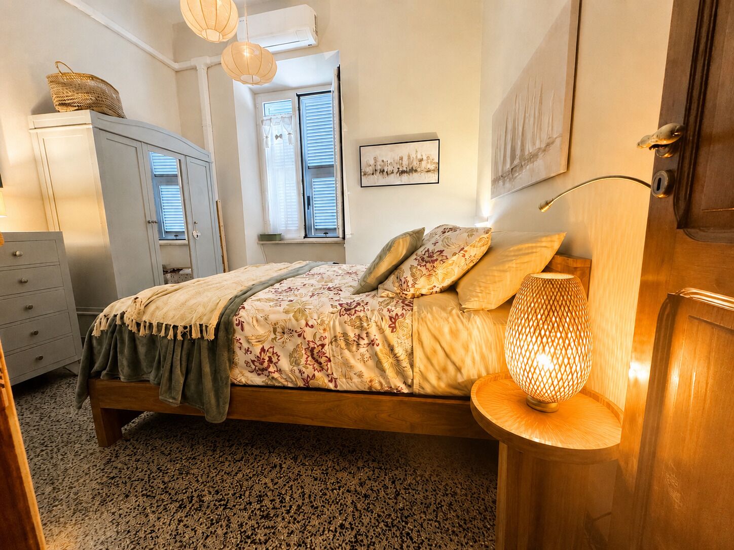 A bedroom with a bed, a dresser, a lamp, and a window with blinds.