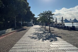 Un paseo empedrado con bancos, sombrillas y mesas junto a la orilla.