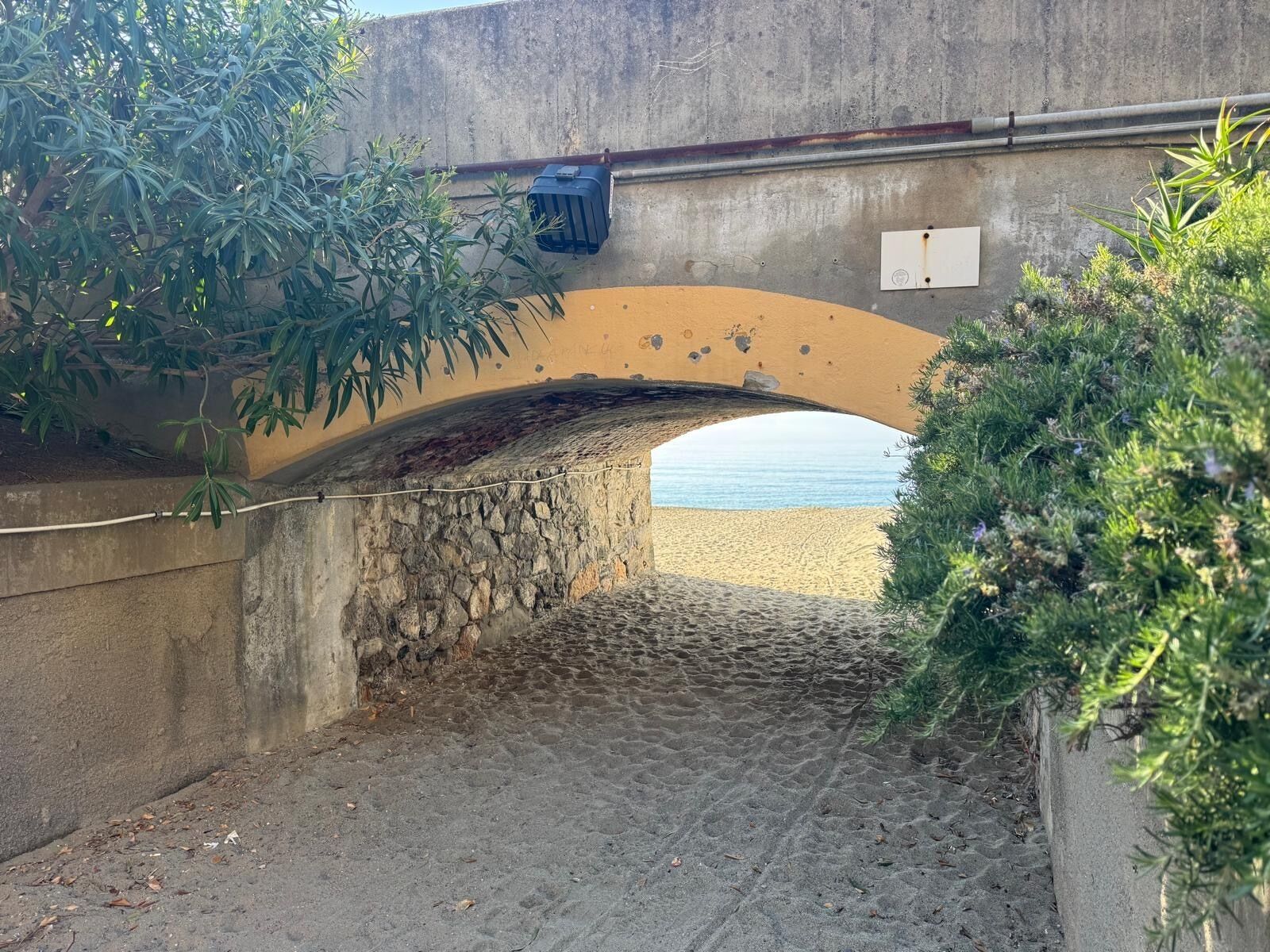 A stone arch bridge over a cobblestone path leading to a beach.