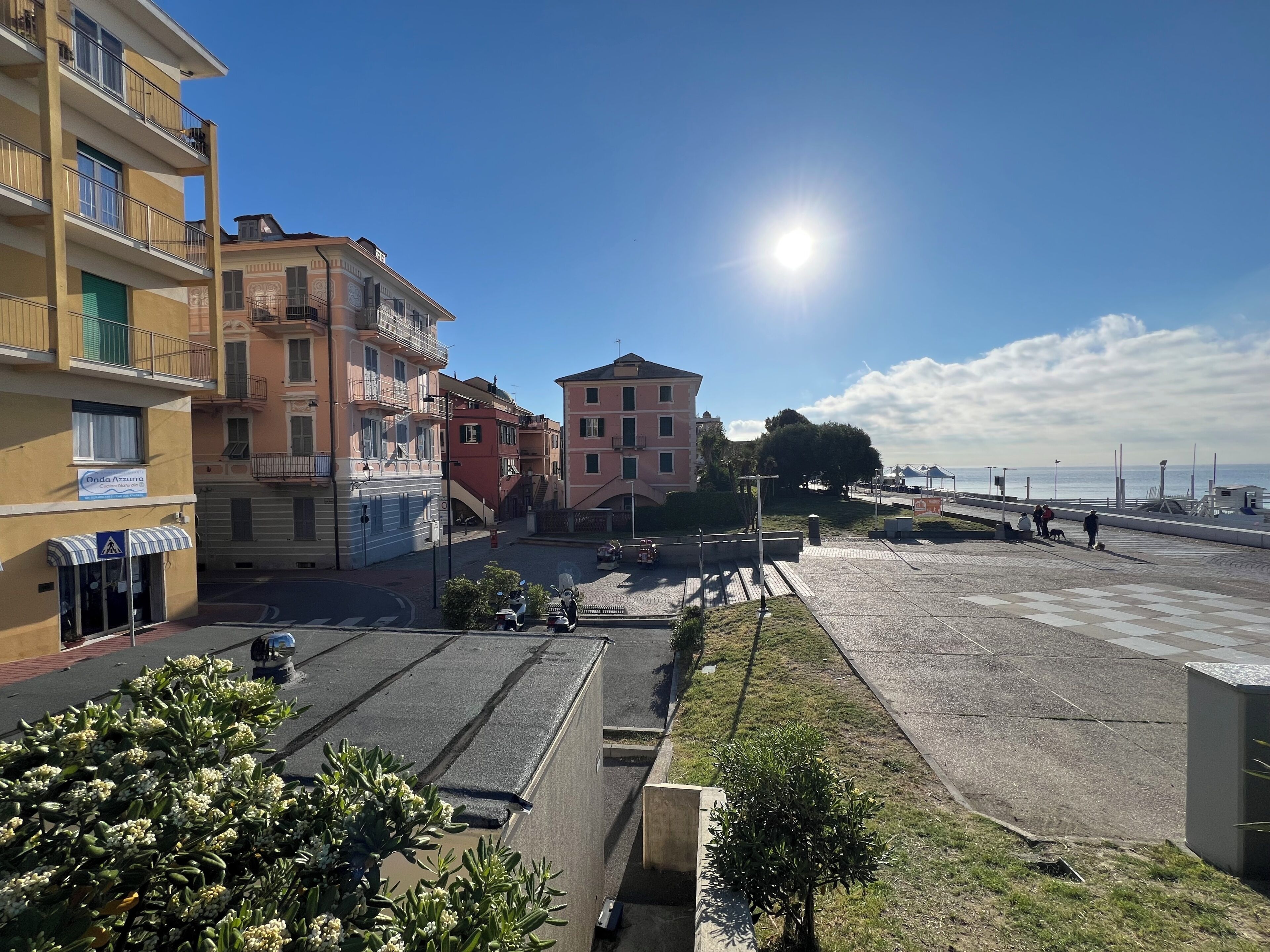 Uma área urbana costeira com edifícios altos, um passeio pavimentado e céu claro.