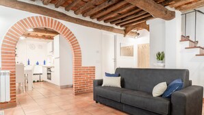 Una sala de estar con un sofá gris oscuro, un arco de ladrillo y una cocina al fondo.