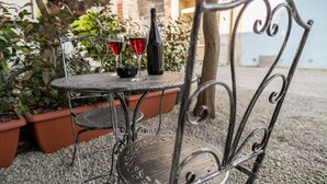Mesa metálica al aire libre con dos copas de vino y una botella, rodeada de plantas en macetas.