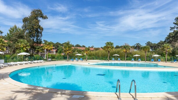 A large, clear swimming pool with lounge chairs and umbrellas, surrounded by greenery and trees. - Cozy Duplex House With Pool (Sérignan)
