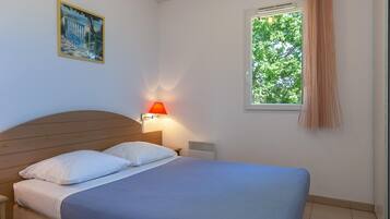 A bedroom with a bed, nightstand, lamp, window, and a painting on the wall.